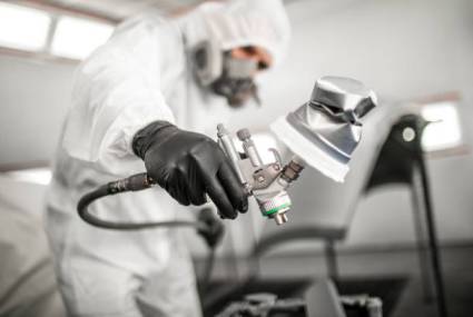 Professional car painter blasting a car part with a base coat paint in a workshop.